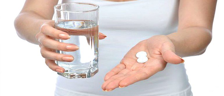 Женщина с двумя таблетками и стаканом воды в руках